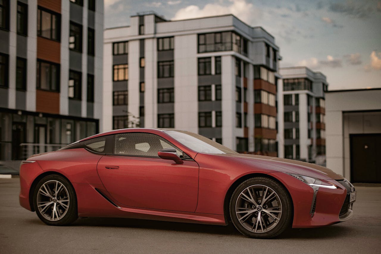 our-journey-01 A sleek luxury red sports car is parked in a modern urban area, showcasing elegance and speed.